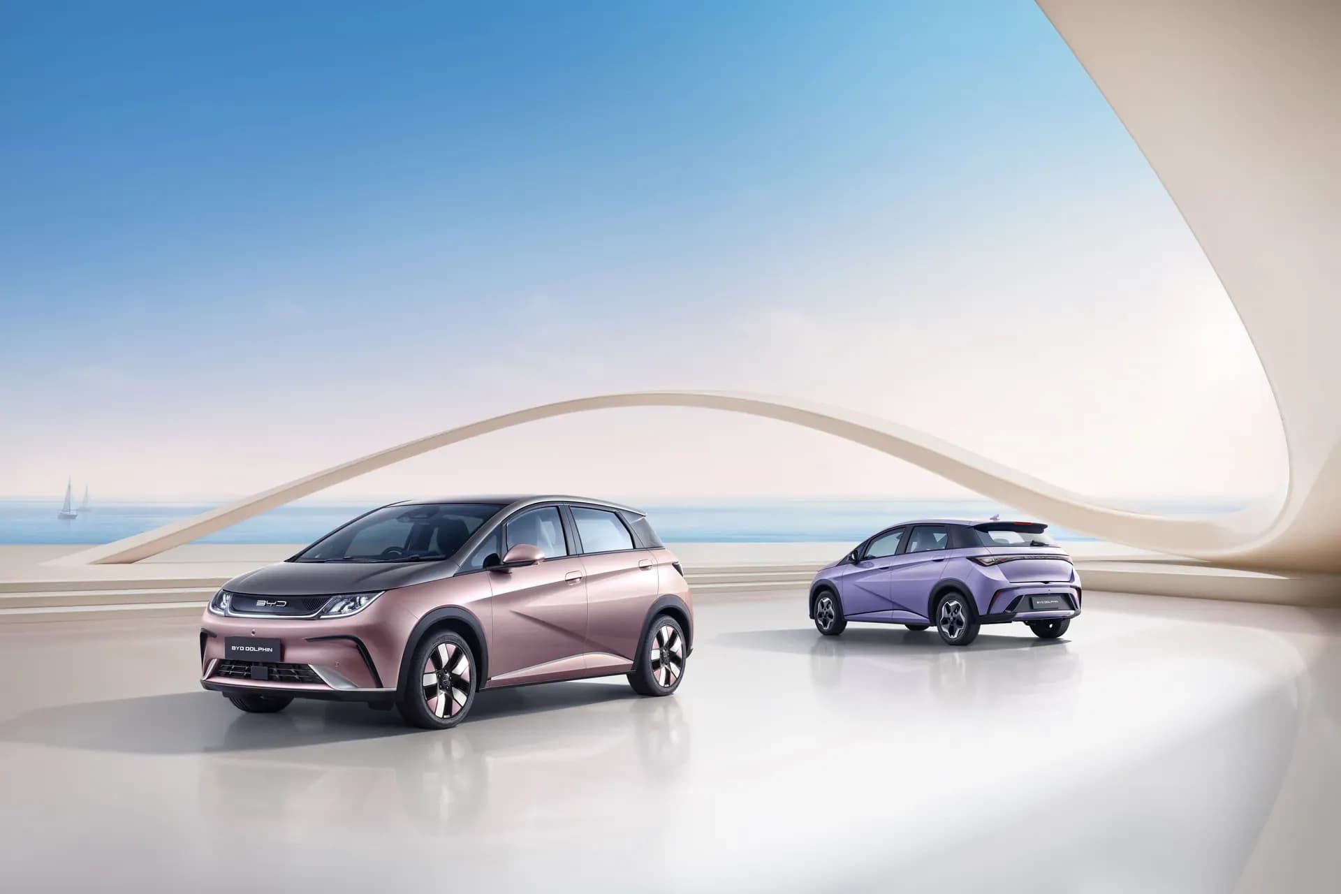 Dua unit BYD Dolphin warna Coral Pink + Urban Grey dan Maldive Purple di area terbuka dengan latar laut
