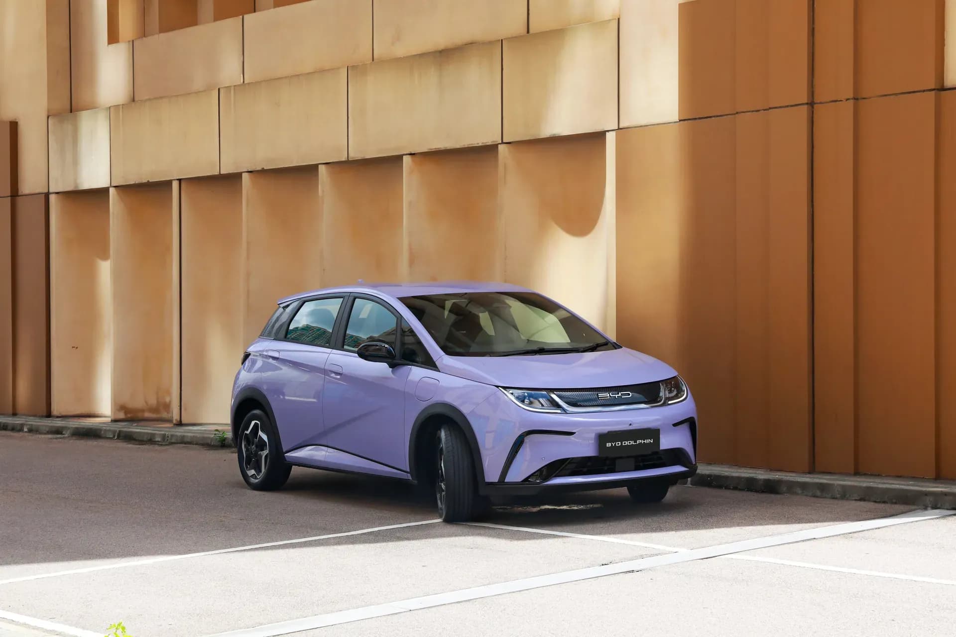 BYD Dolphin warna Maldive Purple diparkir di depan dinding bangunan berwarna jingga