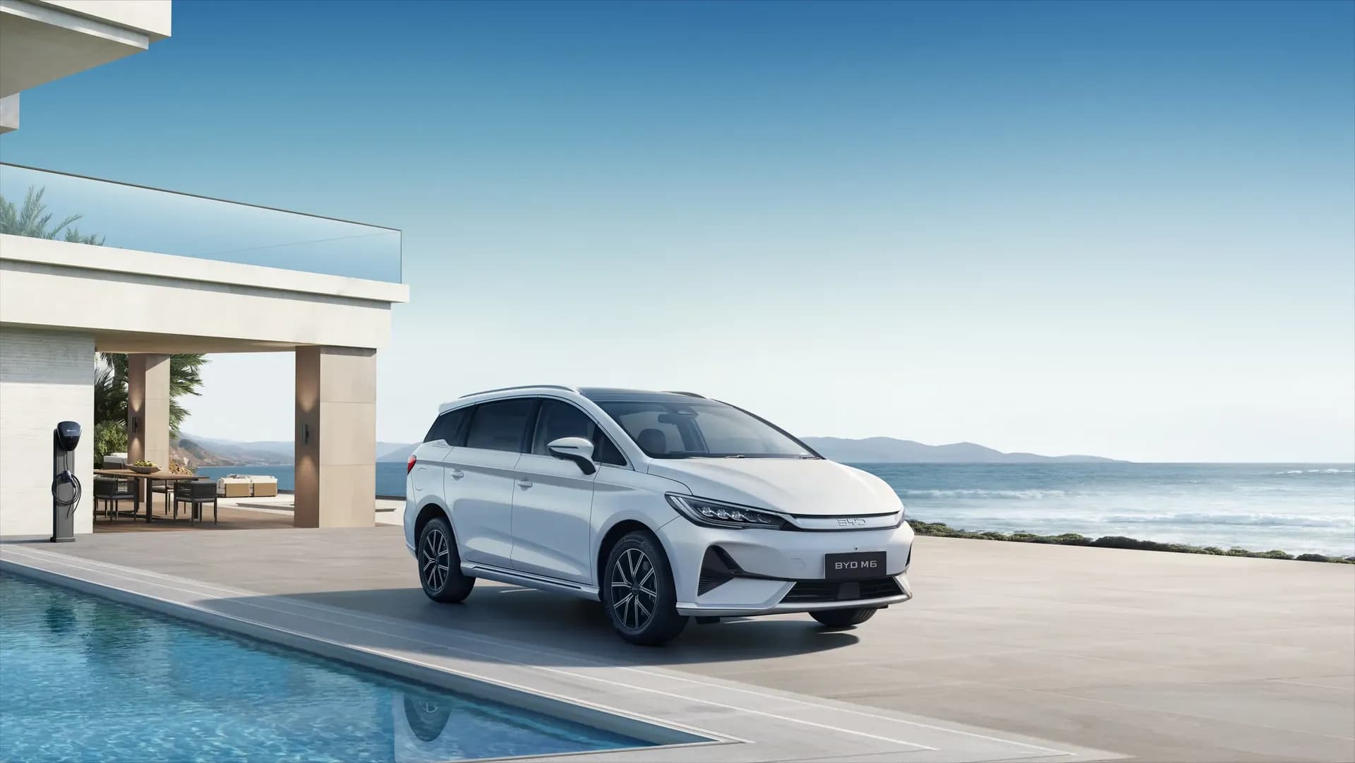 BYD M6 warna Crystal White terparkir di samping vila tepi pantai