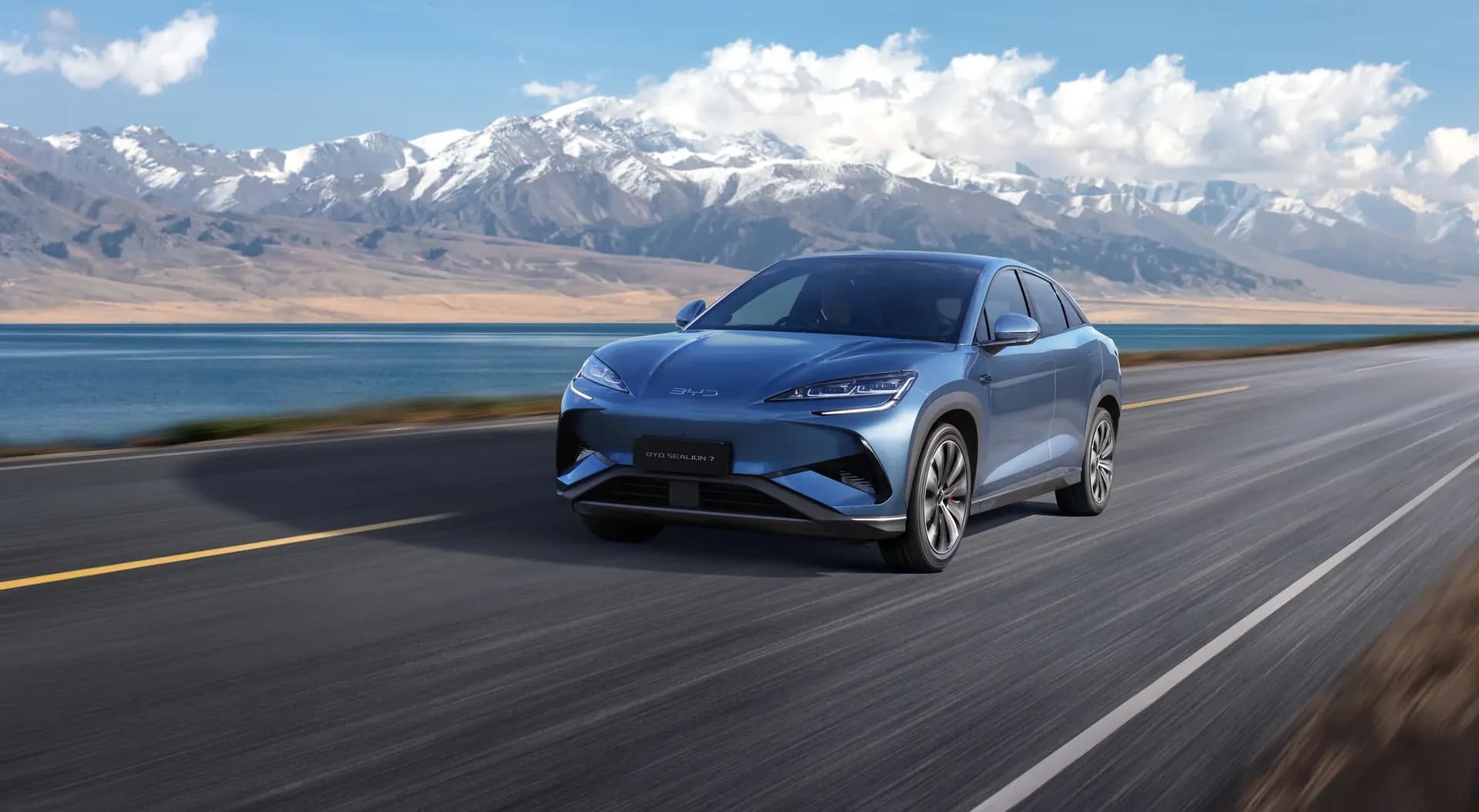 BYD Sealion 7 warna Atlantis Gray melaju di jalan tepi danau dengan latar pegunungan bersalju